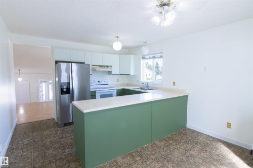 Modern kitchen featuring a striking sage green island with white quartz countertop, stainless steel refrigerator, and ample counter workspace - 4903 11A Avenue Nw, Edmonton, AB - Indoor Photo Showing Kitchen With Double Sink