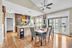 Kitchen and dining area featuring wood-finish flooring, dark wood cabinetry, and a kitchen island with a light-toned countertop and wood-paneled base - 