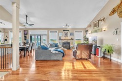 Spacious open-concept interior featuring wood-finish flooring, a stone-clad fireplace, and multiple windows - 