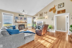 Living area featuring vaulted ceilings, light wood-finish flooring, a stone-faced fireplace, and multiple windows - 