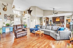 Spacious living area featuring high vaulted ceilings, natural wood-finish flooring, and an open-concept design to the kitchen - 