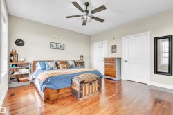 Spacious bedroom featuring wood-finish flooring, light-toned walls, a ceiling fan with integrated lighting, and white paneled doors - 