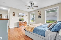 Spacious room featuring wood-finish flooring, two large windows, a ceiling fan with integrated lighting, and neutral wall tones - 