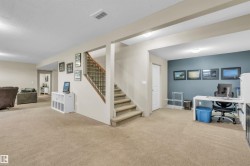 Carpeted lower level featuring a staircase with wood handrail and black metal spindles, a dedicated office area with a distinctive accent wall, recessed lighting, and a white interior door - 