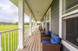 Expansive covered porch featuring a wood-finish floor, white railing, and white columns - 