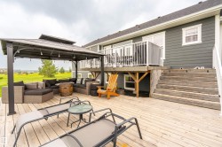 Expansive wood-finish deck with a covered gazebo featuring string lights, a full-length staircase, and access to an upper-level balcony with white railings - 
