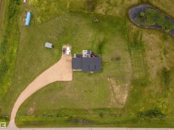 Aerial overview of a single-family residence featuring a dark-toned roof, an expansive gravel driveway, and a partially wooded perimeter - 