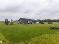 Expansive green lot featuring a dark gray residence with a black roof, a rear deck, and multiple outbuildings - 