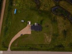 Expansive property featuring a gravel driveway, a large green space, and a dark-roofed structure with an exterior patio area - 