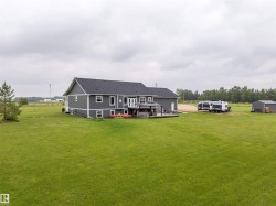 Spacious property featuring a contemporary gray exterior with white trim, a dark shingled roof, a ground-level deck with a gazebo, a gravel driveway, and a detached gray shed - 