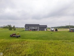 Expansive green lawn surrounds a modern gray residence featuring a dark roof, white window trim, and an elevated rear deck - 