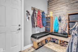 Mudroom featuring built-in L-shaped bench seating with black cushions, overhead wooden storage cubbies, and a distressed wood accent wall - 
