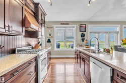 Kitchen featuring rich wood cabinetry, light-toned countertops, hardwood flooring, a gas range, and a built-in dishwasher - 