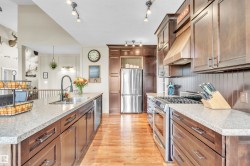 Open-concept kitchen featuring wood-finish flooring, wood cabinetry, stone countertops, and stainless steel appliances - 
