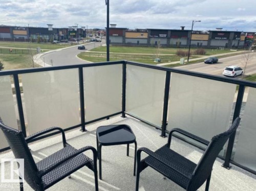 Balcony with dark metal and frosted glass railing, textured flooring, and distant urban buildings - #3 2905 141 St Sw, Edmonton, AB - Outdoor With Balcony