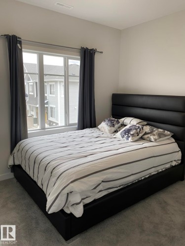 Bright bedroom featuring a large window, soft grey wall paint, and grey carpet flooring - #3 2905 141 St Sw, Edmonton, AB - Indoor Photo Showing Bedroom