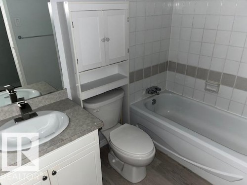 Bathroom featuring a white bathtub, tiled shower surround with accent band, vanity with integrated sink, chrome faucet, and white storage cabinetry - #202 9929 113 St Nw, Edmonton, AB - Indoor Photo Showing Bathroom