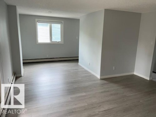 Expansive room featuring wood-finish flooring, light grey painted walls, and a large window with white blinds - #202 9929 113 St Nw, Edmonton, AB - Indoor Photo Showing Other Room