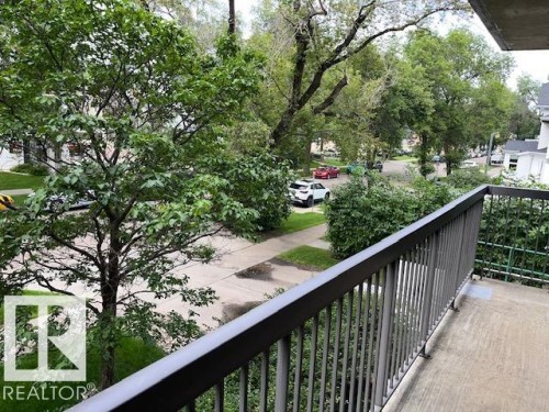 Balcony with a metal railing and concrete flooring, overlooking a street with mature trees and a sidewalk - #202 9929 113 St Nw, Edmonton, AB - Outdoor