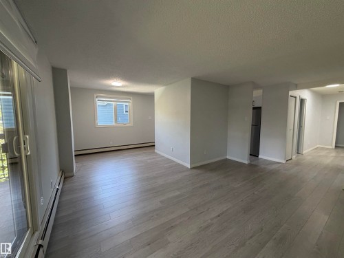Spacious living area featuring wood-finish flooring, a large window, and sliding glass door - #202 9929 113 St Nw, Edmonton, AB 