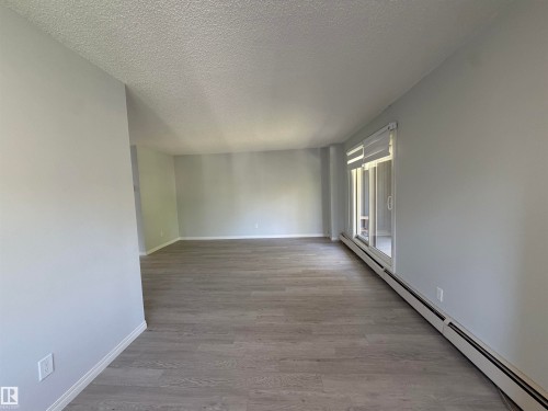 Spacious interior featuring wood-finish flooring, light grey painted walls, and a sliding glass door - #202 9929 113 St Nw, Edmonton, AB 