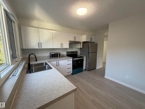 Modern kitchen featuring white cabinetry with dark hardware, stainless steel appliances, a dual basin sink with a gooseneck faucet, and wood-finish flooring - #202 9929 113 St Nw, Edmonton, AB 