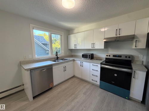 Kitchen featuring stainless steel appliances, dual basin sink with matte black faucet, light wood-finish flooring, white cabinetry, and light-toned countertops - #202 9929 113 St Nw, Edmonton, AB 