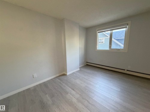 Light wood-finish flooring, white trim, and a window with a roller shade - #202 9929 113 St Nw, Edmonton, AB 