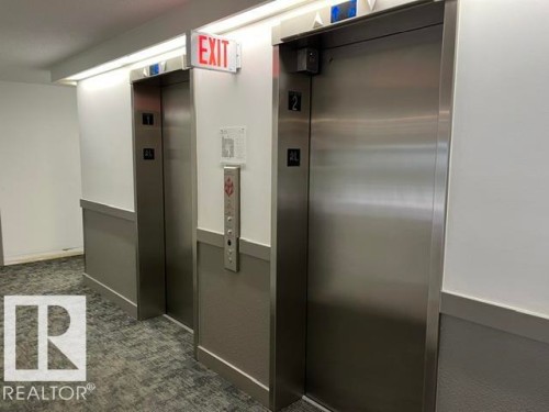 Two stainless steel elevators with call buttons, an emergency exit sign, and recessed lighting - #202 9929 113 St Nw, Edmonton, AB - Indoor Photo Showing Other Room