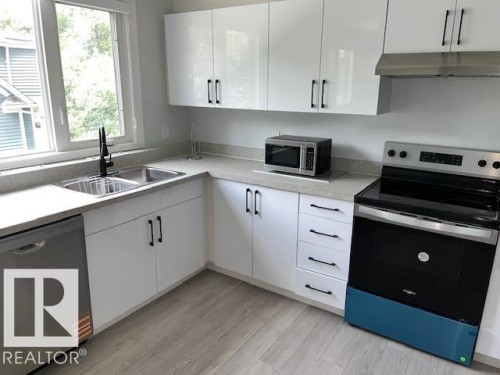 White cabinetry with matte black hardware, stainless steel sink with a black pull-down faucet, light-toned countertops, and wood-finish flooring - #202 9929 113 St Nw, Edmonton, AB - Indoor Photo Showing Kitchen With Double Sink