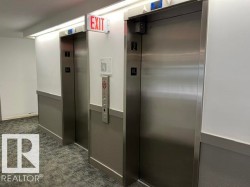 Two stainless steel elevators with call buttons, an emergency exit sign, and recessed lighting - 