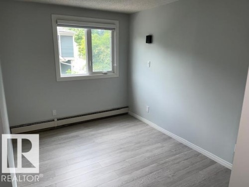 Wood-finish flooring, light gray wall paint, baseboard heating, window with a white frame, and a white ceiling - #202 9929 113 St Nw, Edmonton, AB - Indoor Photo Showing Other Room