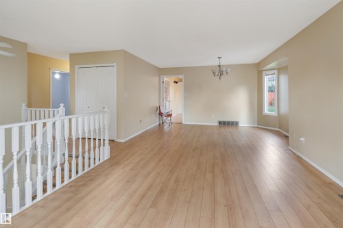 Expansive room featuring wood-finish flooring, a contemporary chandelier, a bay window, and a white baluster staircase - 1055 Jones Crescent Nw, Edmonton, AB - Indoor Photo Showing Other Room