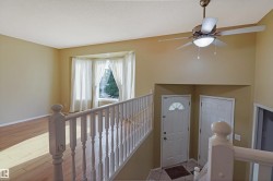Upper-level landing featuring hardwood flooring, wooden stair railing with turned balusters, ceiling fan with integrated lighting, and access to multiple rooms - 