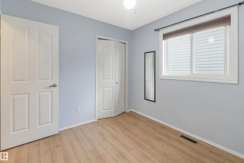 Bright bedroom featuring wood-finish flooring, soft blue-gray walls, and large window with plantation shutters and natural light - 1055 Jones Crescent Nw, Edmonton, AB - Indoor Photo Showing Other Room