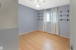 Bright and airy bedroom with fresh periwinkle walls, wood-finish flooring throughout, and abundant natural light from large windows dressed in neutral curtains - 