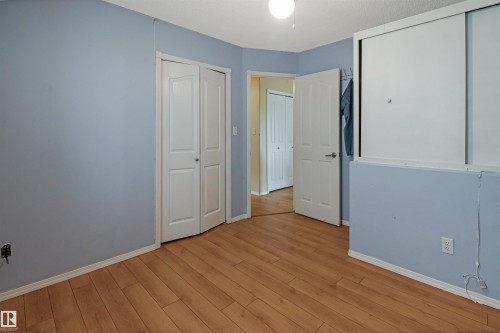 Spacious bedroom with soft blue walls, warm wood-finish flooring, and multiple closet options including mirrored sliding door storage - 1055 Jones Crescent Nw, Edmonton, AB - Indoor Photo Showing Other Room