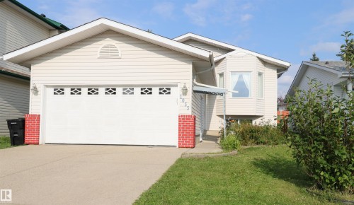 Exterior featuring light-colored siding, a prominent attached garage with decorative window inserts, a bay window with a small awning, and a concrete driveway - 1055 Jones Crescent Nw, Edmonton, AB - Outdoor