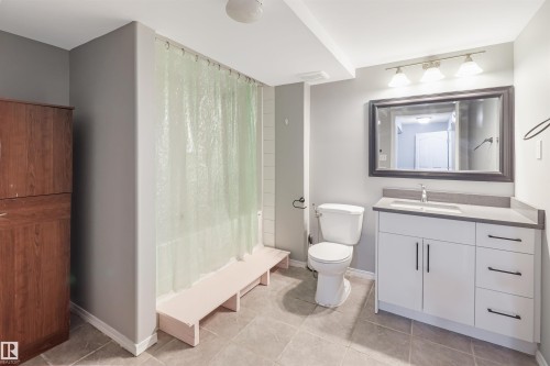 Spa-inspired primary bathroom featuring a frameless glass-enclosed shower with pale green tile surround, floating vanity with soft-close cabinetry and brushed nickel hardware, large illuminated mirror, and neutral tile flooring - 1055 Jones Crescent Nw, Edmonton, AB - Indoor Photo Showing Bathroom