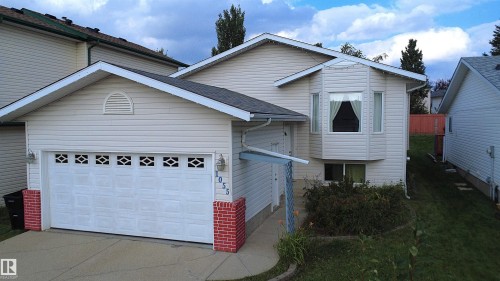 Front exterior featuring light-colored horizontal siding, a white panel garage door with decorative inserts, a bay window, and a concrete driveway - 1055 Jones Crescent Nw, Edmonton, AB - Outdoor With Exterior