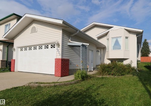 Charming single-story residence featuring a white vinyl exterior, attached garage with paneled door, and pitched rooflines with extended eaves - 1055 Jones Crescent Nw, Edmonton, AB - Outdoor