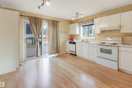 Kitchen featuring wood-finish flooring, white cabinetry, white appliances, and a sliding glass door providing exterior access - 1055 Jones Crescent Nw, Edmonton, AB - Indoor Photo Showing Kitchen With Double Sink