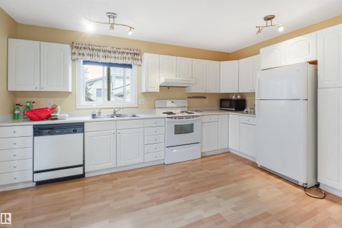 Spacious kitchen featuring white cabinetry with ample storage, wood-finish flooring throughout, stainless steel appliances including a gas range and dishwasher, and a large refrigerator - 1055 Jones Crescent Nw, Edmonton, AB - Indoor Photo Showing Kitchen With Double Sink