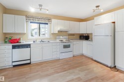 Spacious kitchen featuring white cabinetry with ample storage, wood-finish flooring throughout, stainless steel appliances including a gas range and dishwasher, and a large refrigerator - 