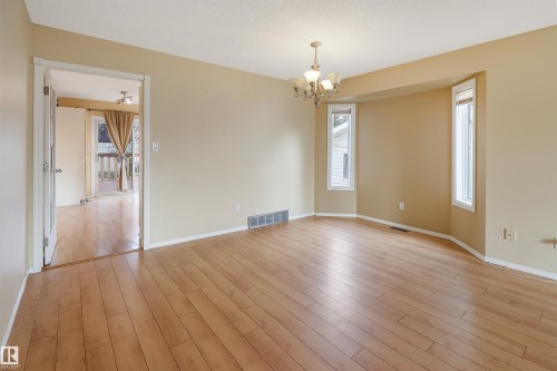 Spacious living room showcasing gleaming wood-finish flooring, warm neutral walls, and abundant natural light from multiple windows - 1055 Jones Crescent Nw, Edmonton, AB - Indoor Photo Showing Other Room