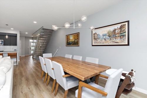 Open-concept living space with wood-finish flooring, a modern chandelier, and a glass-paneled staircase - 3241 Kulay Way Sw, Edmonton, AB - Indoor Photo Showing Dining Room