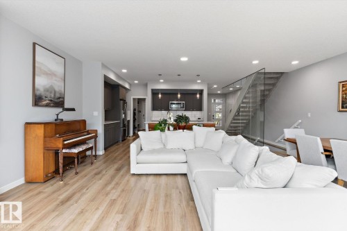 Open-concept living area with wood-finish flooring, recessed lighting, and a glass-paneled staircase - 3241 Kulay Way Sw, Edmonton, AB - Indoor Photo Showing Living Room