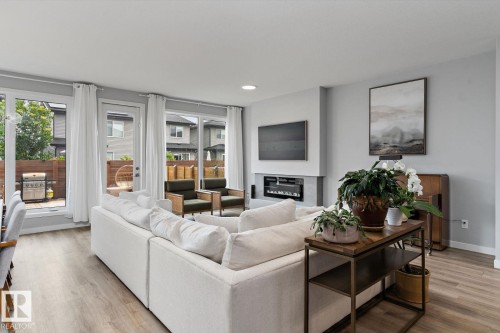 Open-concept living area featuring a built-in linear fireplace, wood-finish flooring, and multiple glass doors leading to an outdoor patio - 3241 Kulay Way Sw, Edmonton, AB - Indoor Photo Showing Living Room With Fireplace