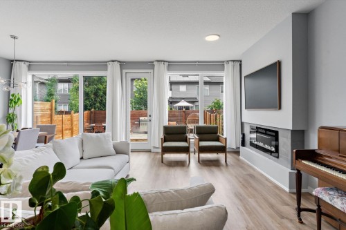 Expansive living area with wood-finish flooring, a linear electric fireplace, and a wall-mounted television - 3241 Kulay Way Sw, Edmonton, AB - Indoor Photo Showing Living Room With Fireplace