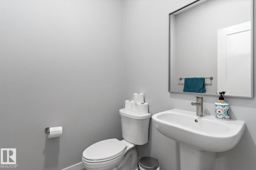 Pedestal sink with a single-handle faucet, wall-mounted mirror, and a contemporary toilet - 3241 Kulay Way Sw, Edmonton, AB - Indoor Photo Showing Bathroom